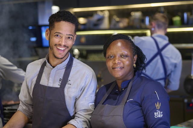 Chef Binta and a teammate, both in aprons, smiling together in the kitchen.