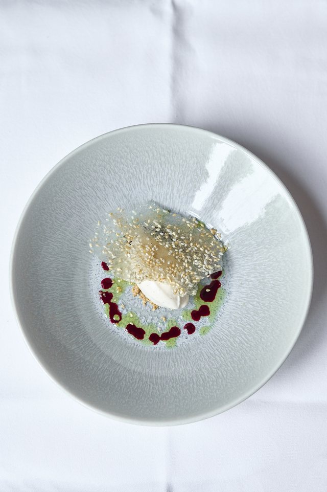 Looking straight down at a pale plate: a dessert with a bright green swoosh, dark berries and a shard of tuile.