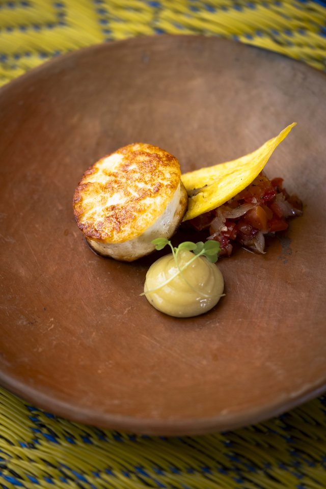 Looking down at a dark clay plate: a seared scallop-like piece beside a smear of yellow purée.