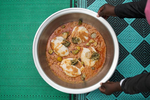 Overhead view of a bowl of stew with shrimp, held over a teal patterned cloth.