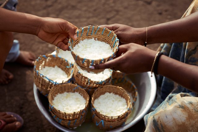 Hands passing woven baskets full of white fonio flour between each other.