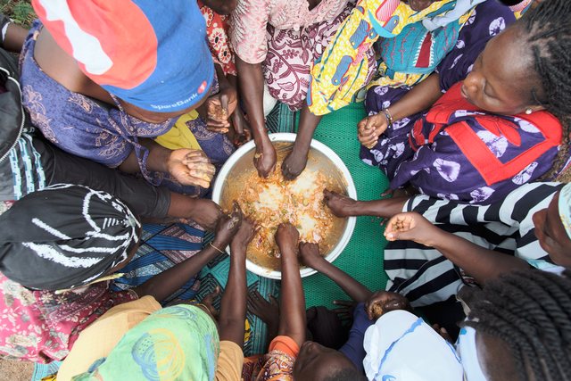 Looking straight down at many hands gathered around a mound of grain on the ground.