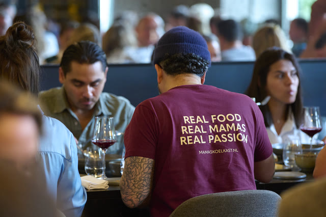 Seen from behind, a member of the dining room wearing a shirt reading Real Food, Real Mamas, Real Passion.