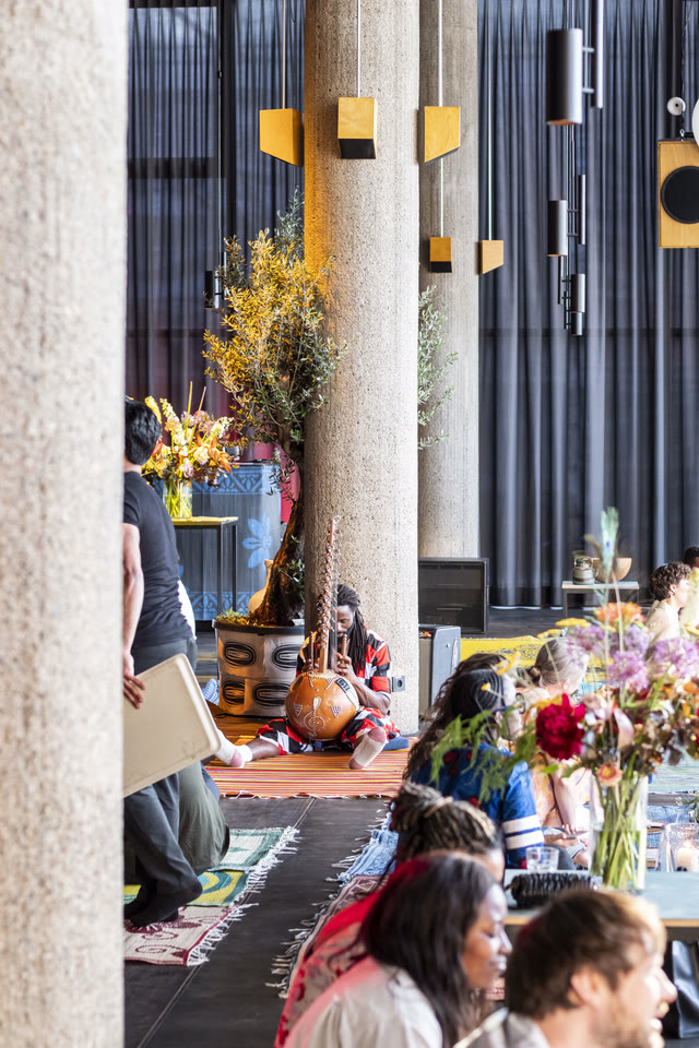 Guests seated on the floor of a room with concrete columns and framed artwork on the walls.